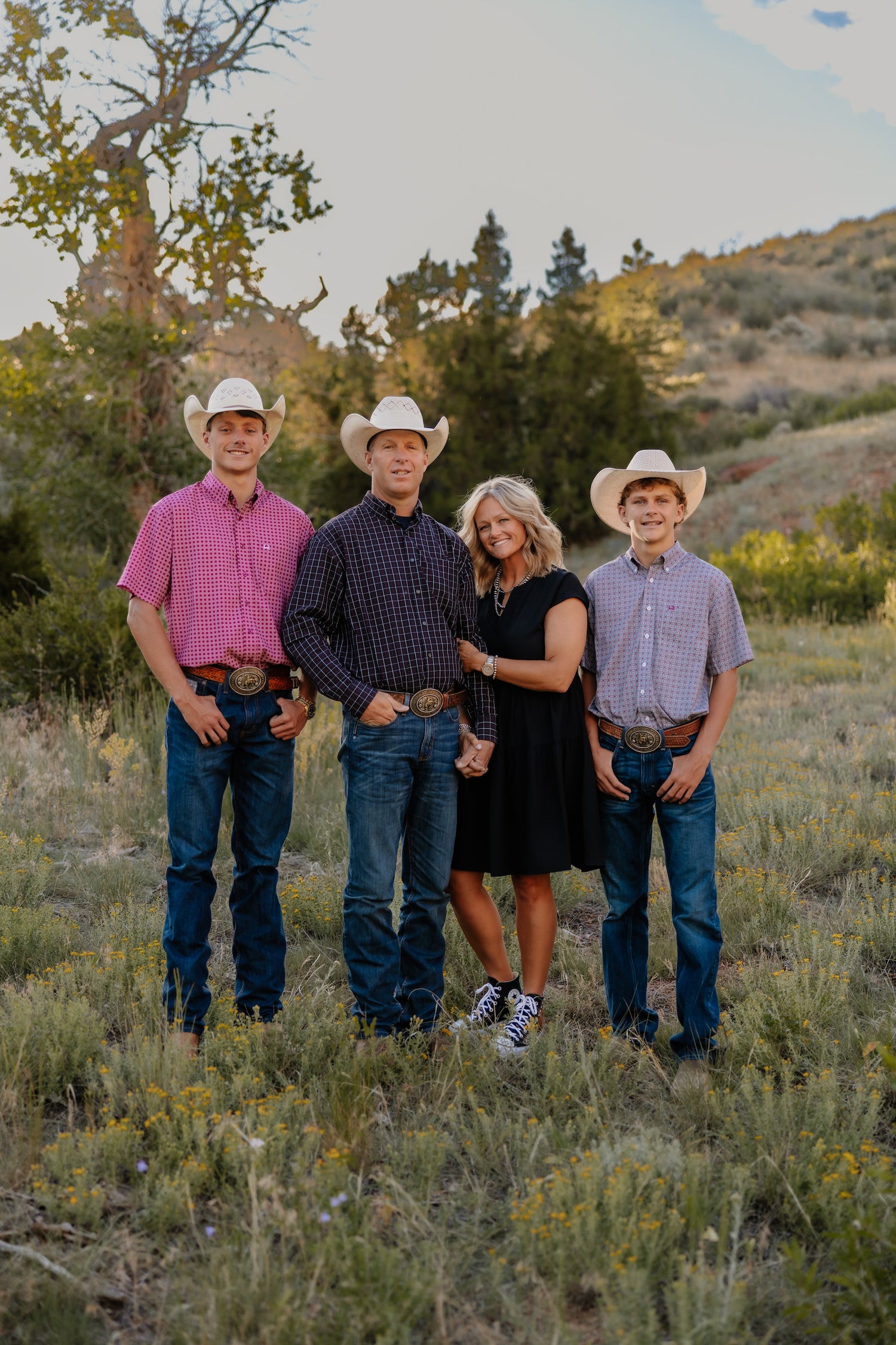 Four people wearing cowboy hats standing in a field with trees and mountains in the background.