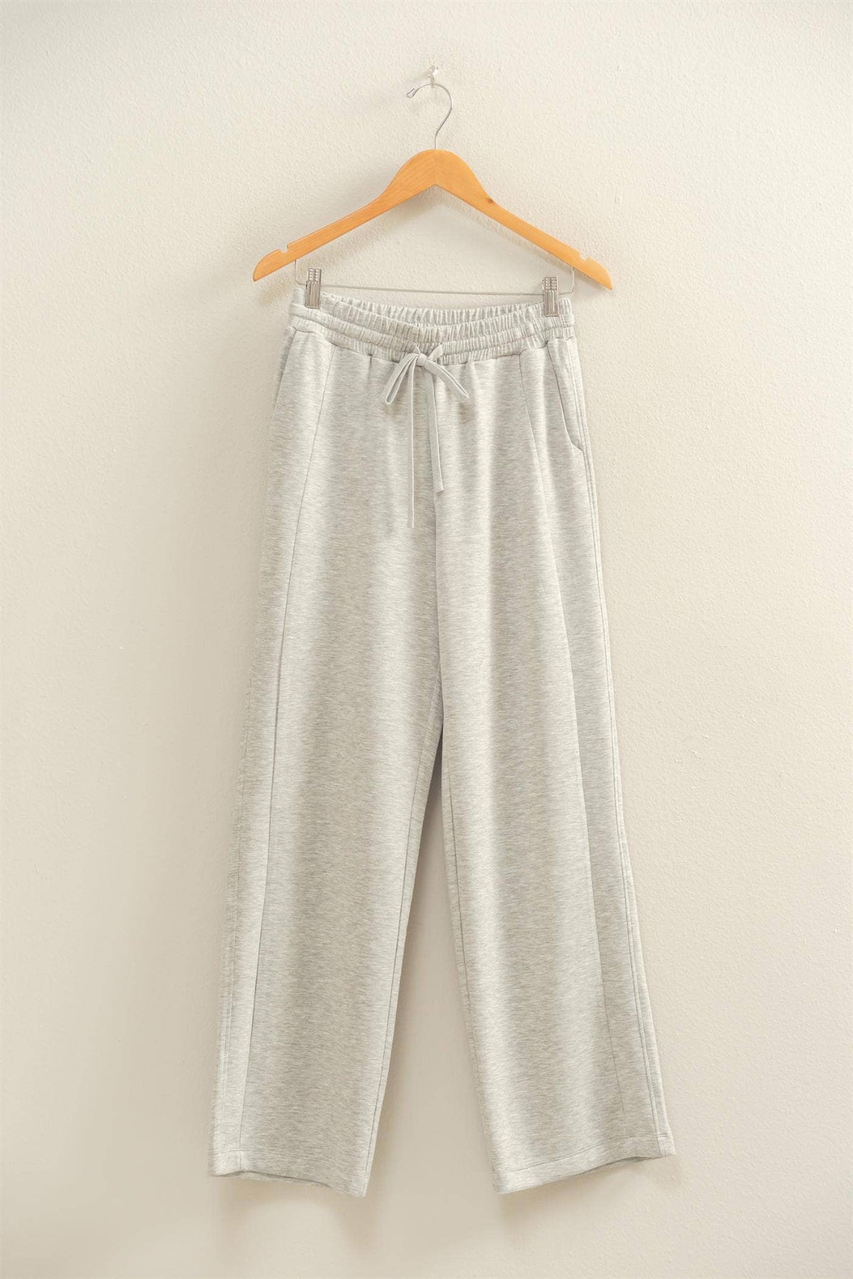 Light gray pants on a wooden hanger against a beige background